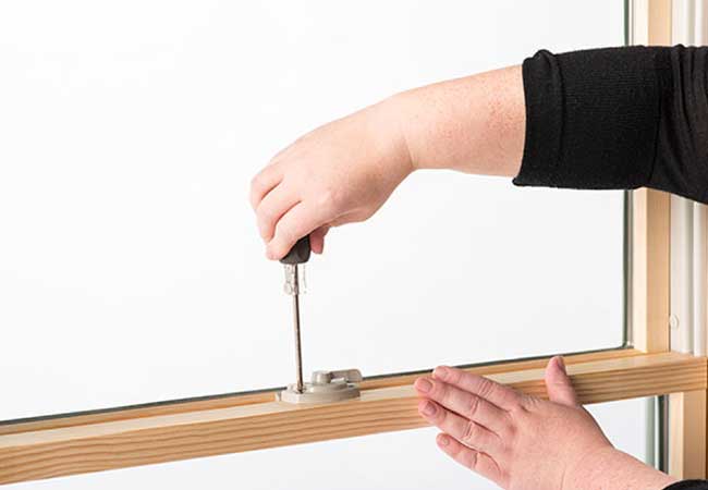 A hand holding a screwdriver to remove window hardware on an unfinished wood window.