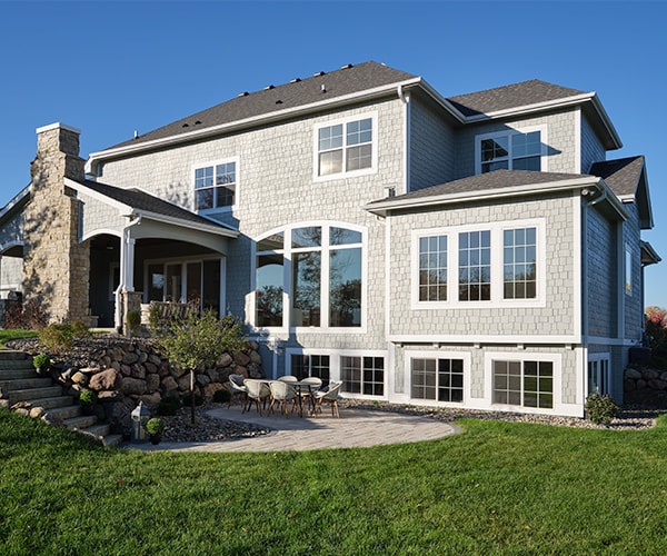 The exterior of a large home that's facing the sun, which is shining into all windows, including several basement sliding windows.