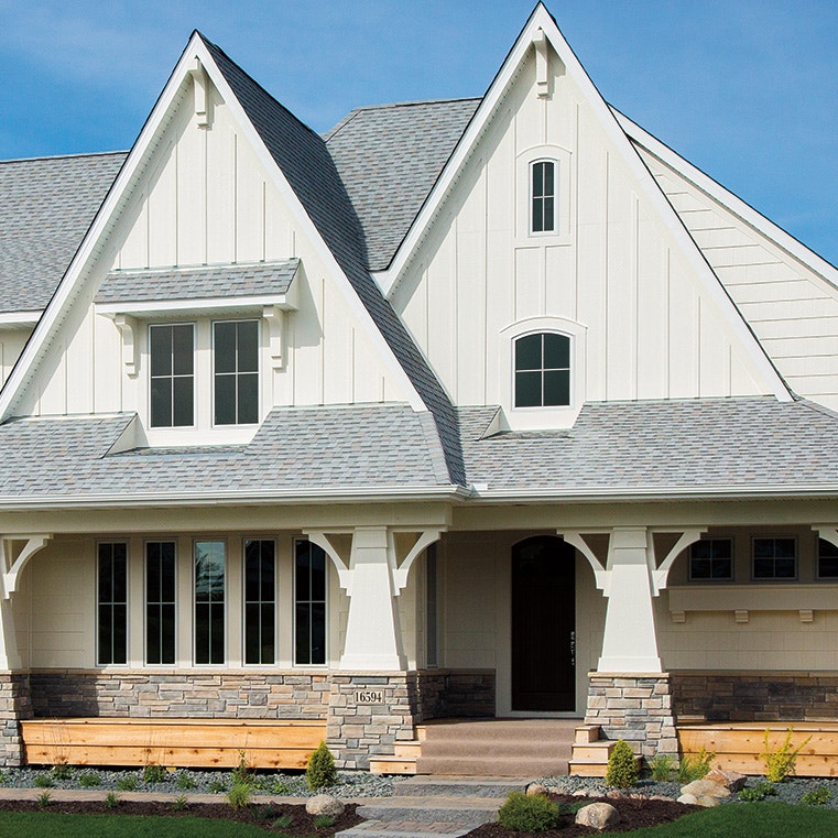 A modern house exterior featuring a white arched window, stone accents, and a gabled roof.
