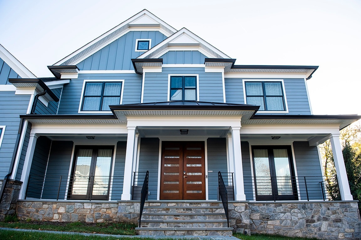 A modern house with black windows and blue siding, featuring a stone porch and wooden front door.