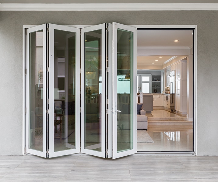 A wood bifold patio door is partially open on a modern gray home exterior.