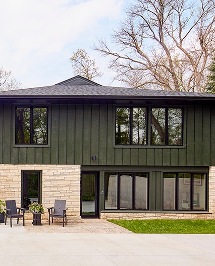 A green split-level home with stone accent walls and black windows.