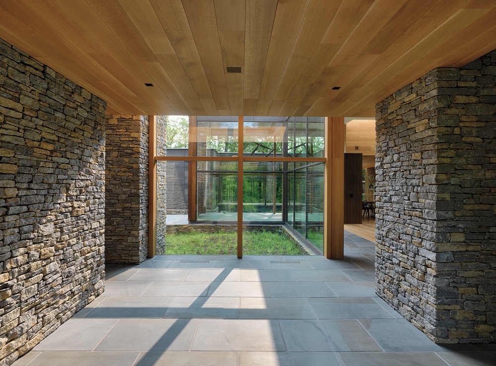 Hallway with stone walls on either side, wood plank ceiling, and wall of picture windows ahead