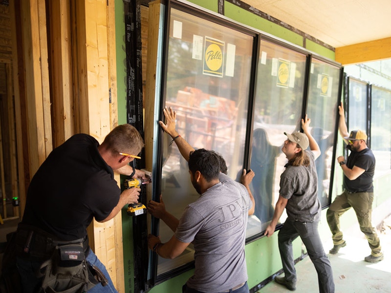 four construction workers installing a three-wide wood window configuration