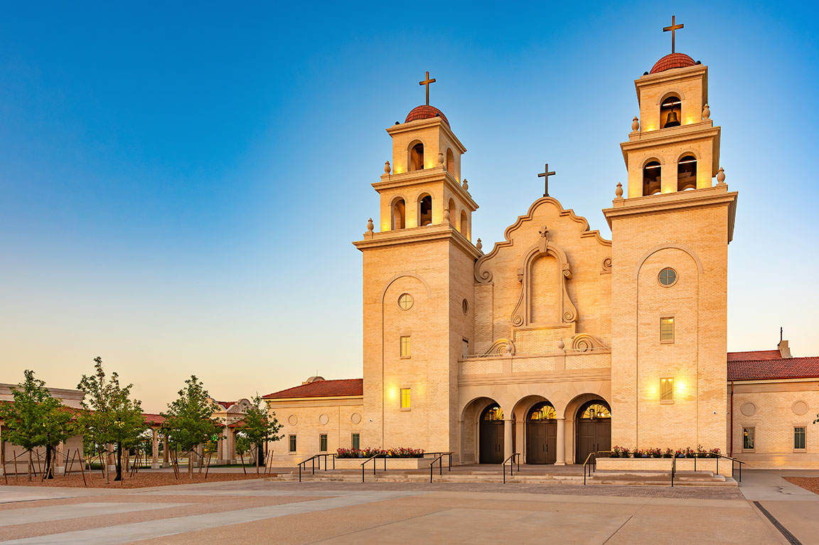 Front view of large church with twin bell towers and crosses at sunset