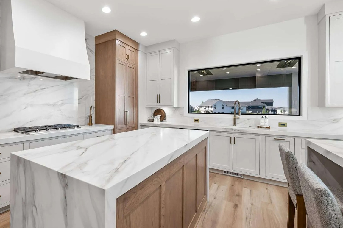 Modern kitchen with marble island, light wood cabinetry, and large picture window.