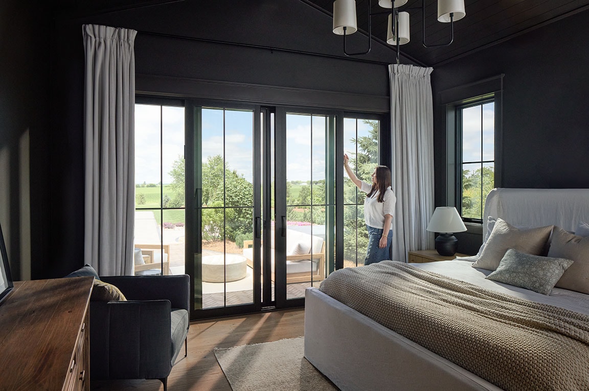 A dark-painted bedroom has a black sliding patio door that opens to a beautiful outdoor patio.