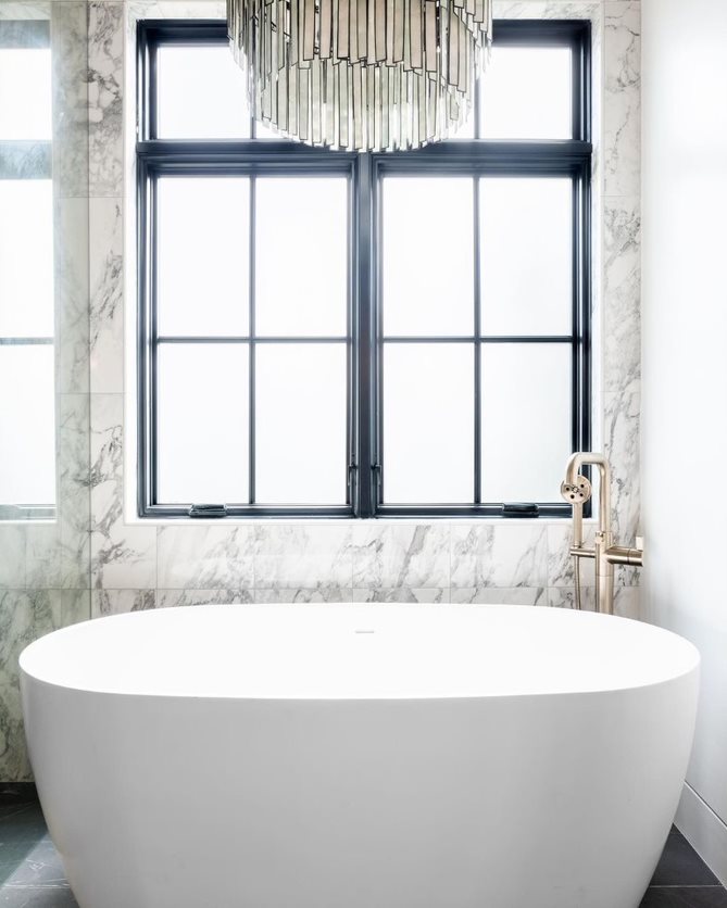 Black casement windows sit behind the bathtub in a modern bathroom.