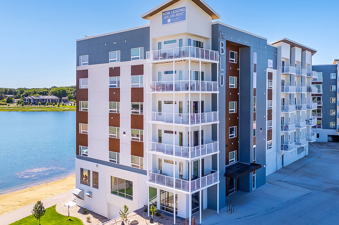 Modern apartment building with large windows and balconies overlooking a lake and fountain.