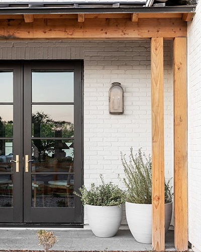 a set of black french doors on a white-brick home exterior with natural wood beams 
