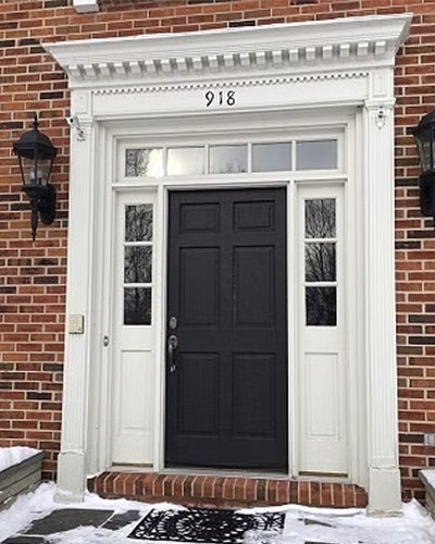 An old wood front door with white framing on a brick home.