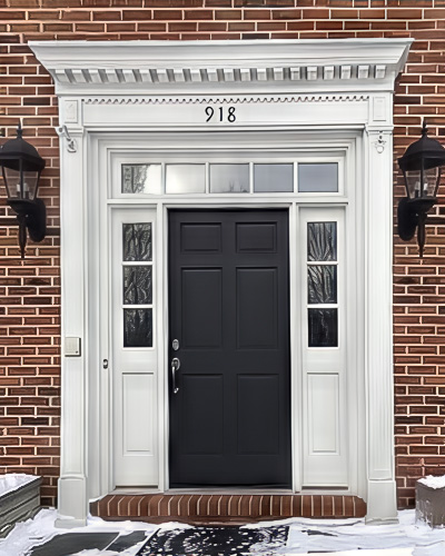 An old wood front door with white framing on a brick home.
