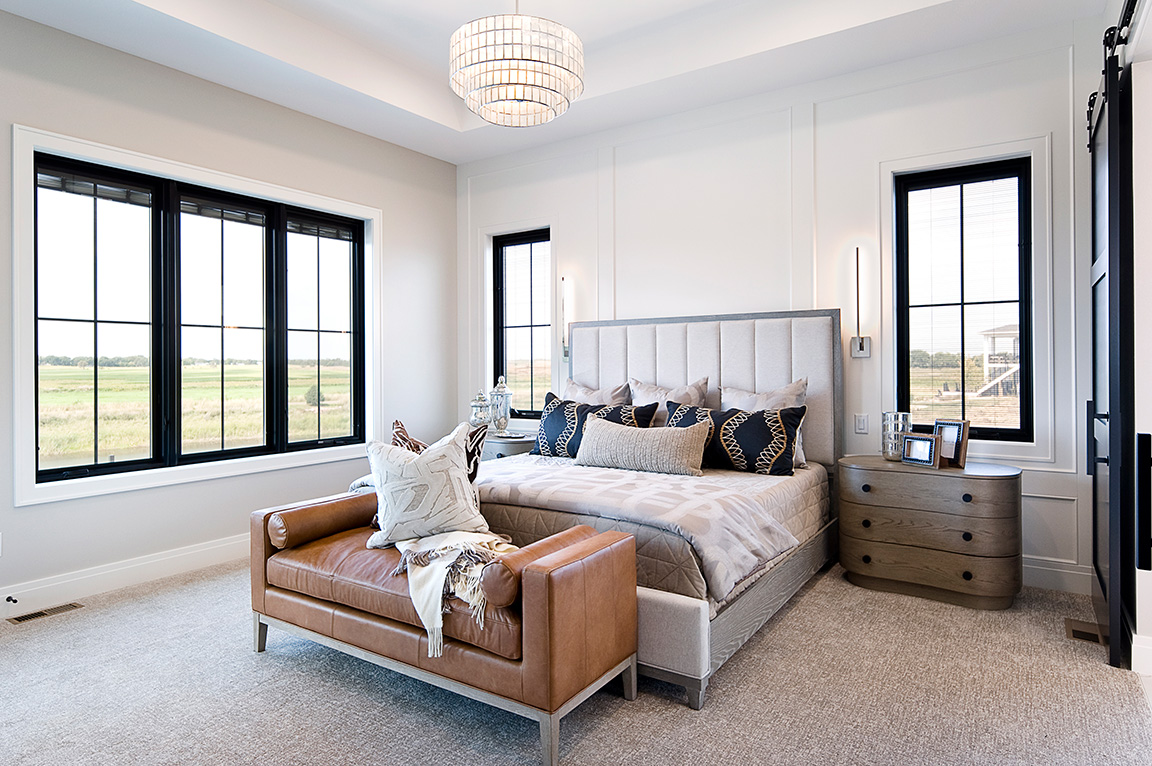 A modern bedroom featuring a stylish bed, leather sofa, and new construction windows with black frames.
