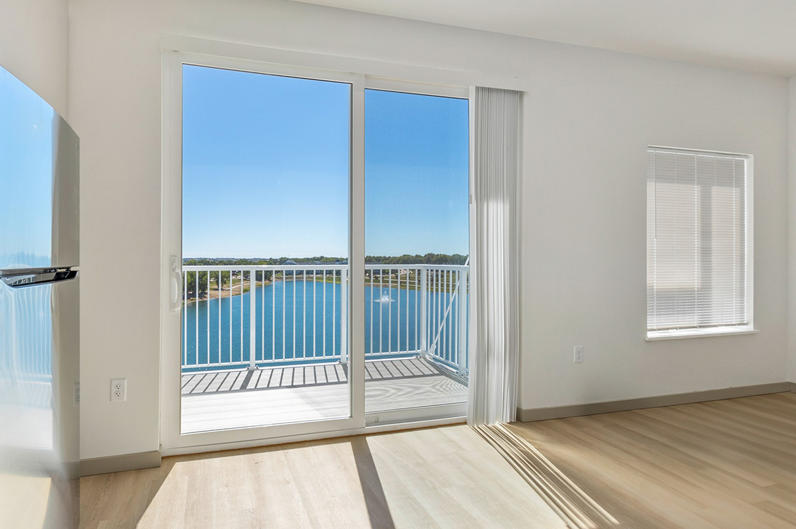 Large apartment windows with a glass door open to a balcony with a clear outdoor view.