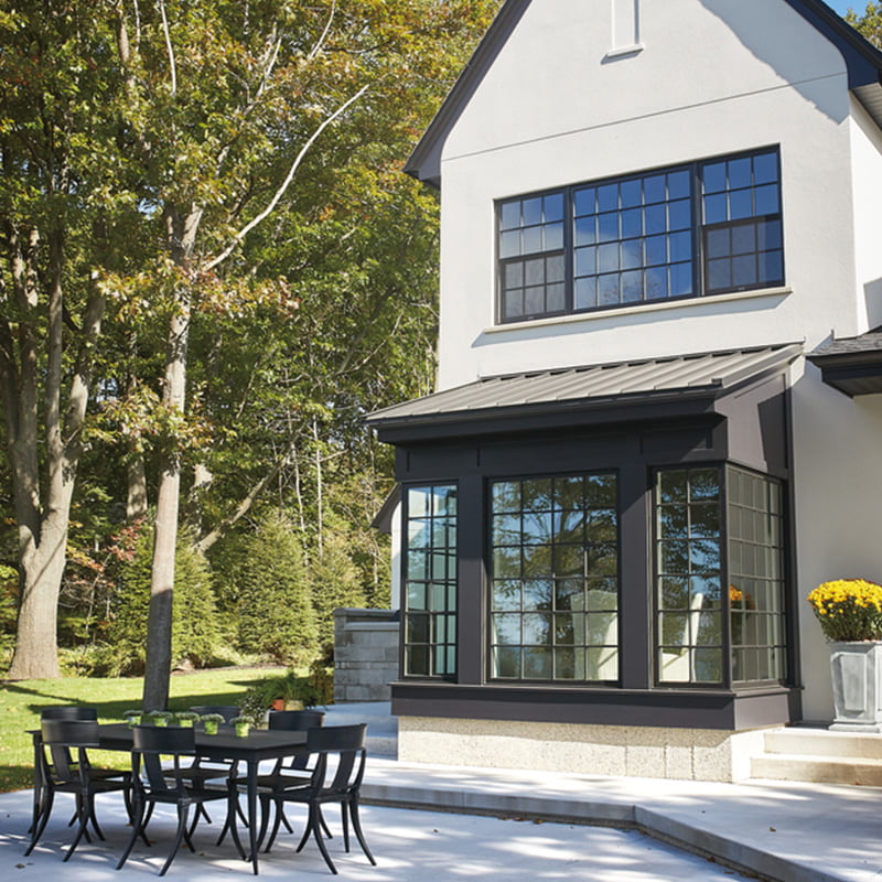 A patio with a dining table looking towards an elegant home with brown windows with traditional grille patterns.