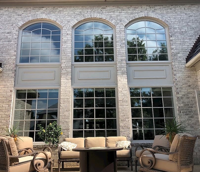 an exterior deck sits in front of an expansive brick home exterior and six large wood windows