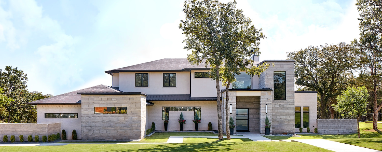 Modern tan and stone house with black windows on green grass
