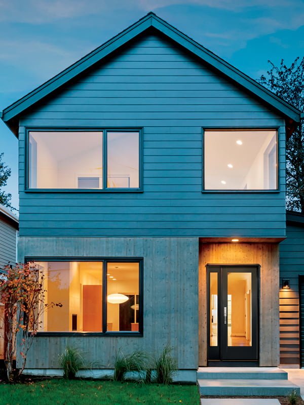Two story home at dusk with a black entry door and wide windows