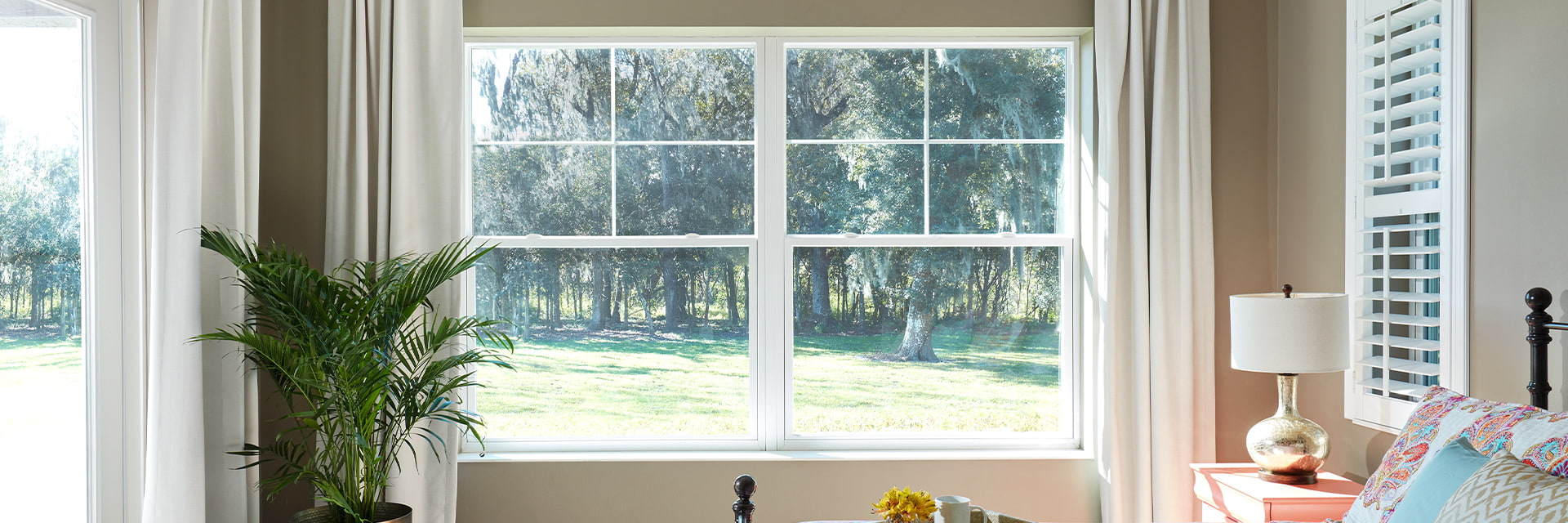 Two single-hung windows open to green trees and grass