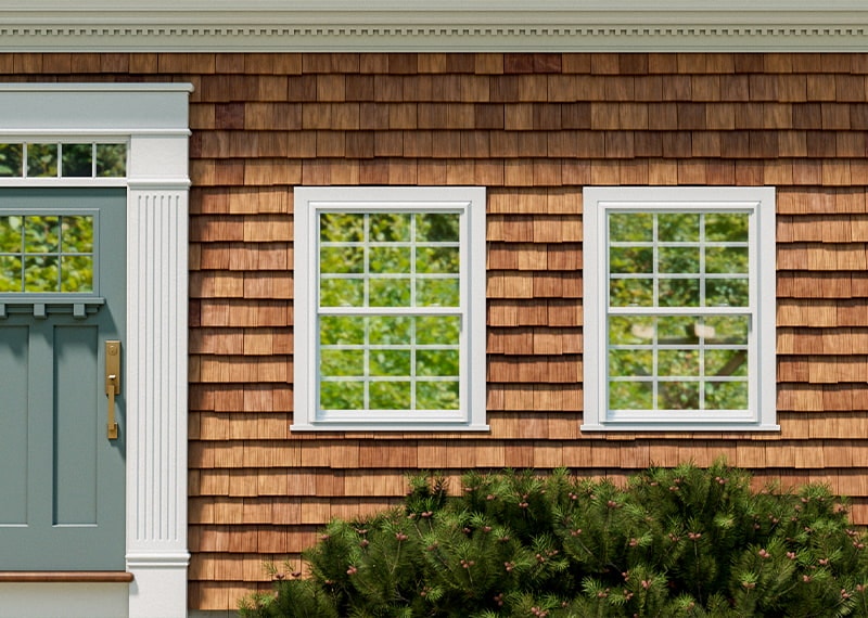 Two traditional single-hung windows on a home exterior with wood siding