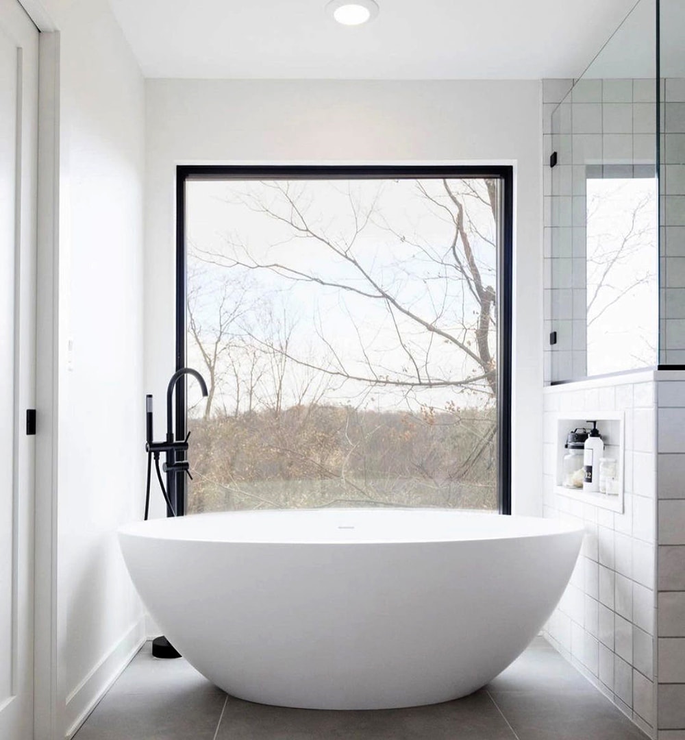 White bathroom features black rectangular window without grilles to  light bathtub area.
