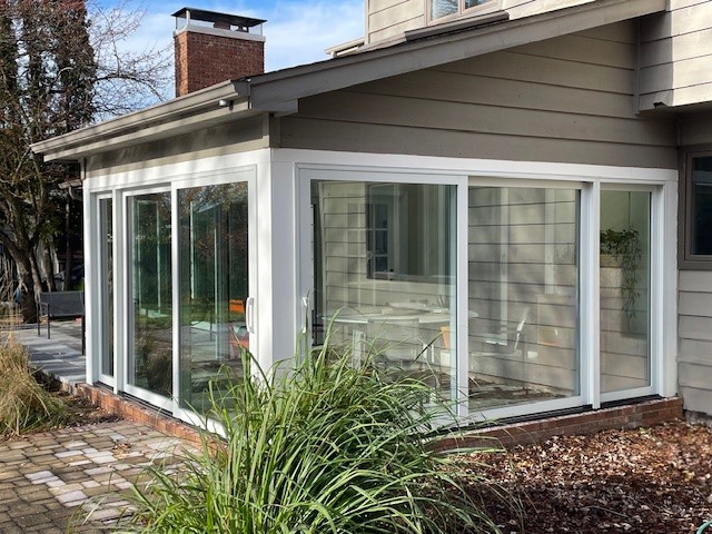 After modern sunroom glass sliding doors, surrounded by greenery. 