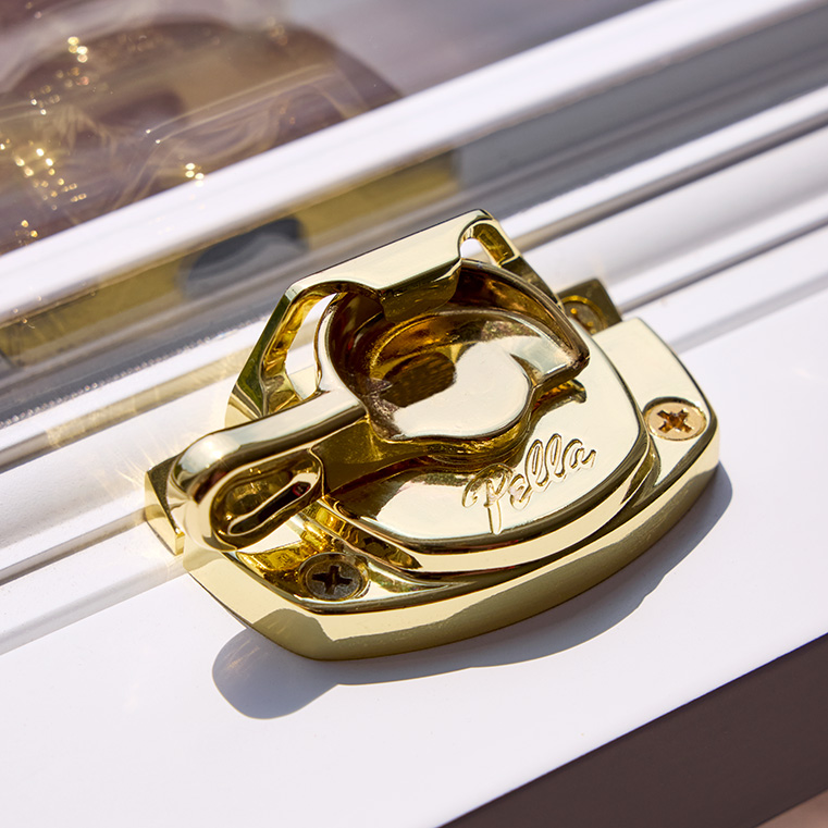 A close-up of a gold spoon-style lock installed on a white window frame. 