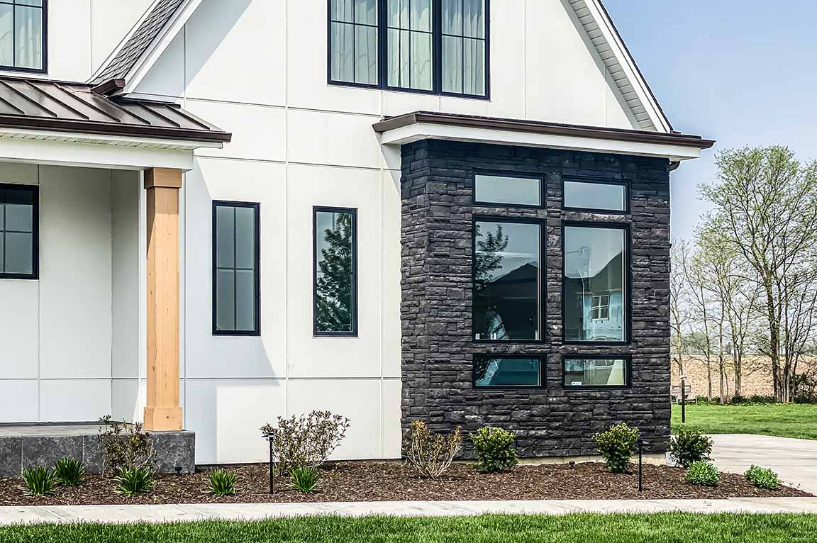 Black farmhouse windows with dark stone exterior and white siding.