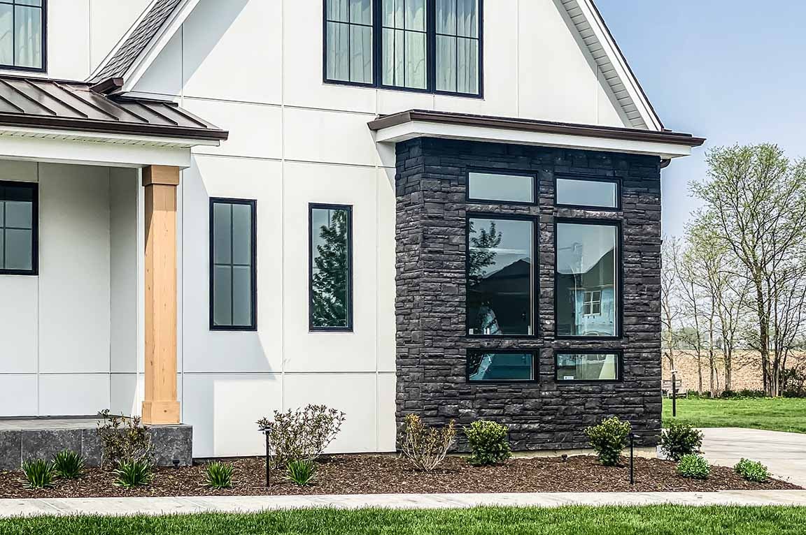 Black farmhouse windows with dark stone exterior and white siding.
