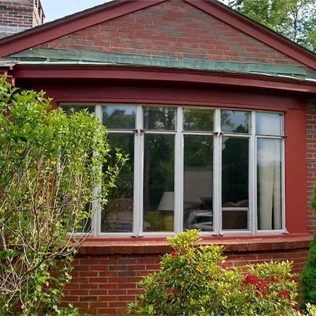 A brick house featuring a bow window surrounded by greenery.