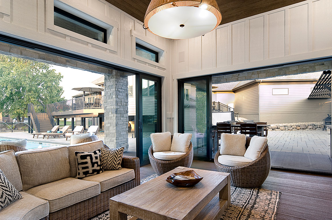 A modern stone pool house with large windows, featuring a patio and outdoor seating area.