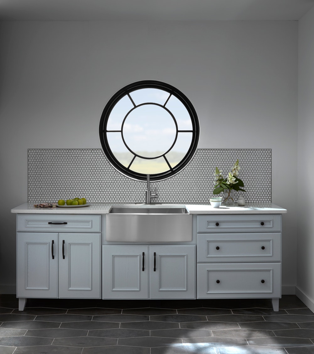 white kitchen counter and sink with black circle window with custom sunburst grilles overhead