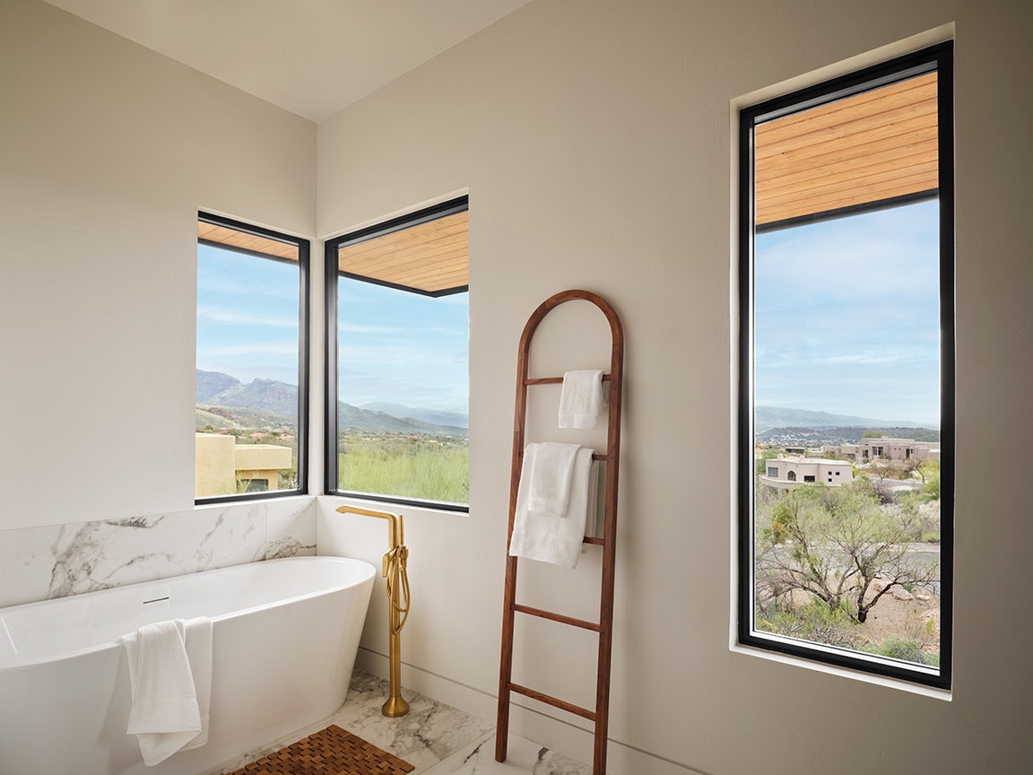Choosing best windows is shown with large picture windows in a modern bathroom overlooking mountains and homes.