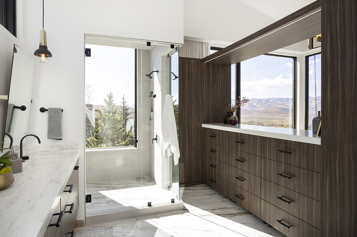 A modern bathroom featuring large windows, a glass shower, and wooden cabinets.