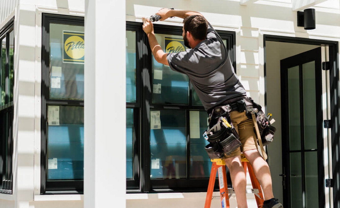 a single contractor applies the finishing sealant to black Pella double-hung windows