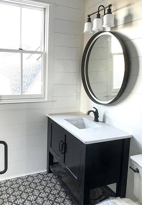 black and white bathroom features white double-hung window and black vanity with black circle mirror above