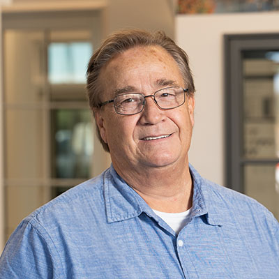 An older man with glasses is wearing a blue shirt with a pocket protector.
