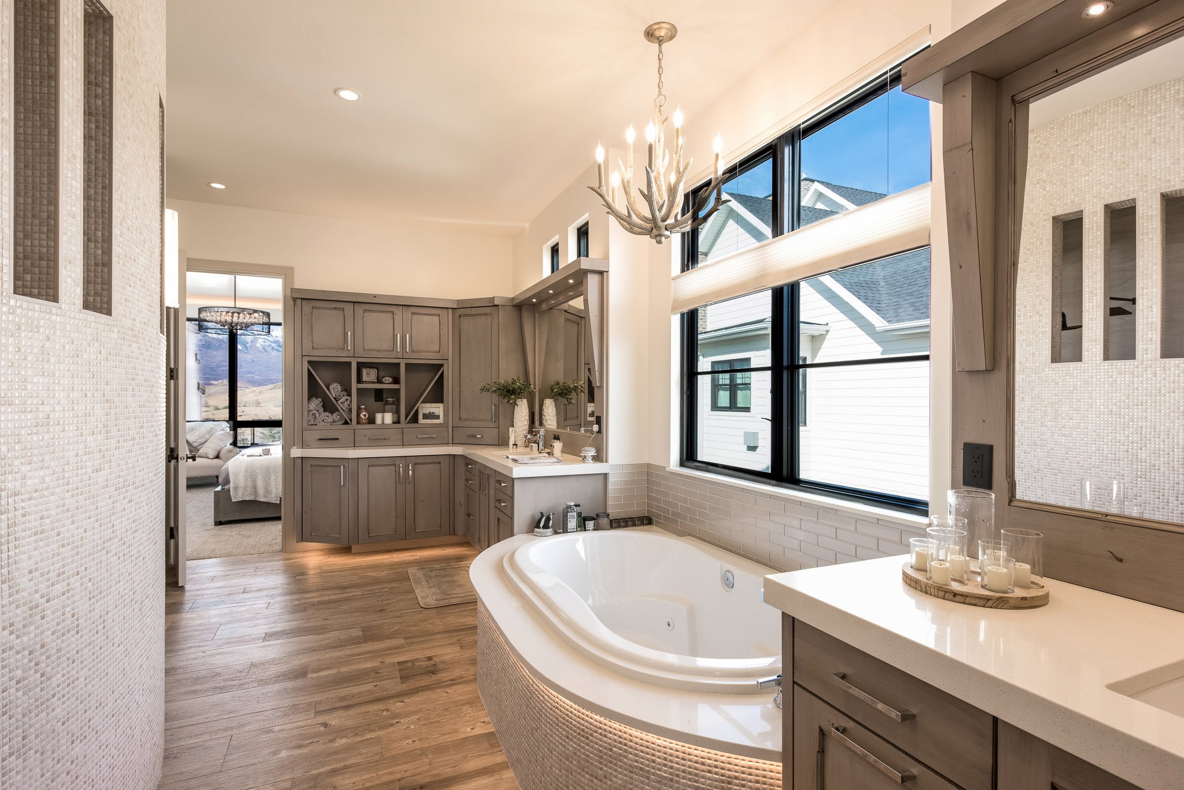 A massive bathroom has black windows over the bathtub, custom taupe-colored cabinetry and a rustic light fixture.