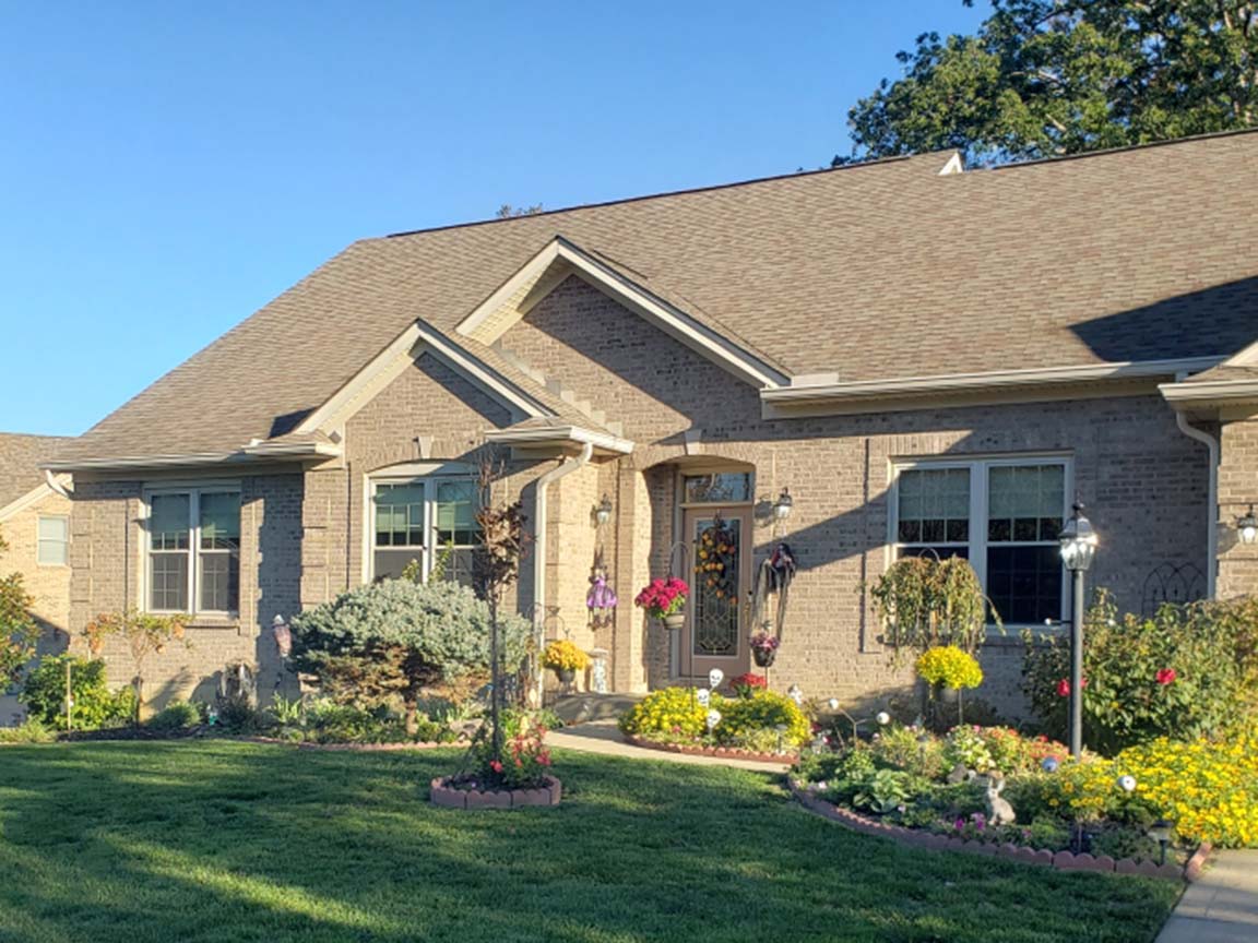Brick home exterior with front windows, landscaped lawn, and garden beds.