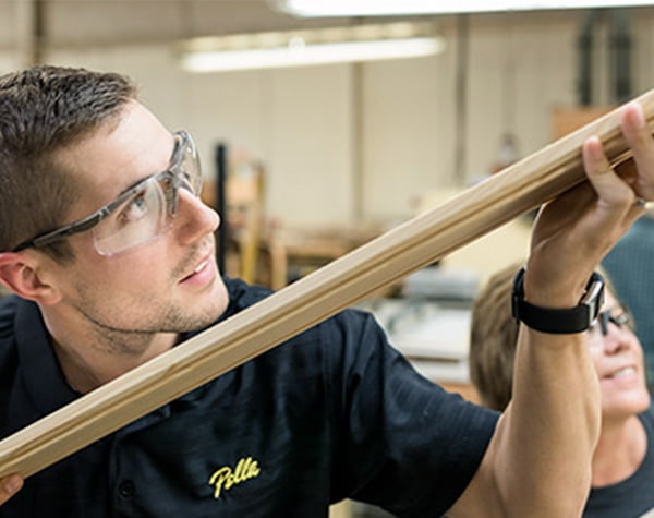 A Pella inspector is checking the quality of a piece of wood trim