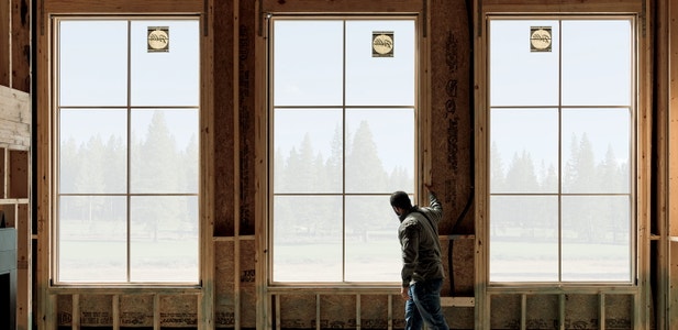 construction worker standing by 3 large windows on the interior of a home under construction