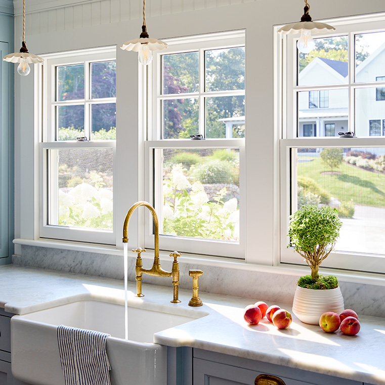 A modern kitchen with a brass faucet, featuring a bright kitchen over-the-sink window.