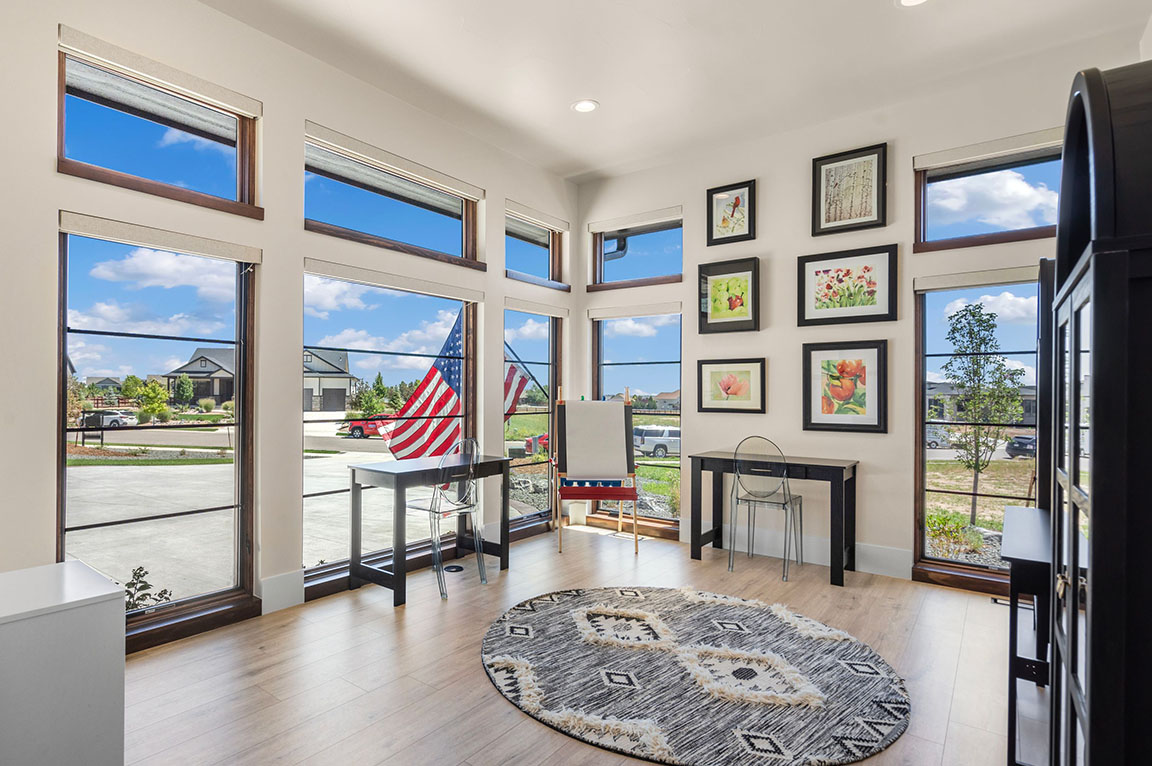 Bright modern home office with large windows, American flag outside, minimalist furniture, and framed botanical artwork on the wall.