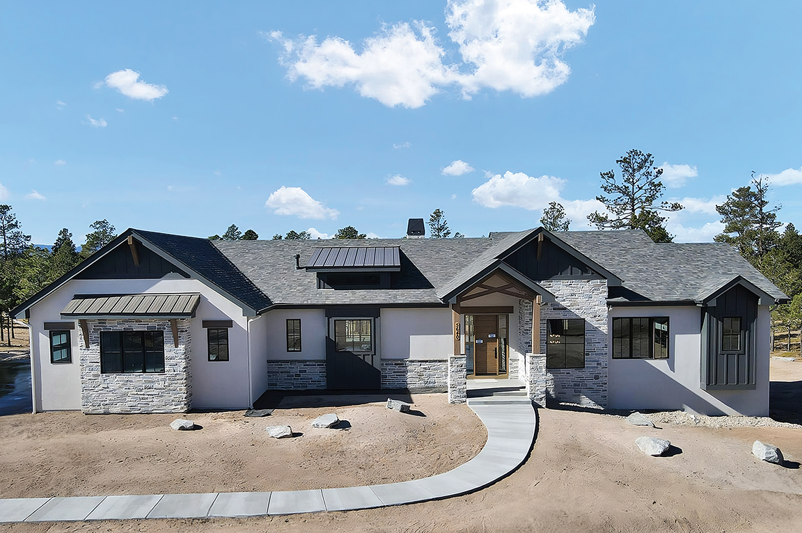 A white mountain home with black windows and a wood patio door with the blue sky overhead.