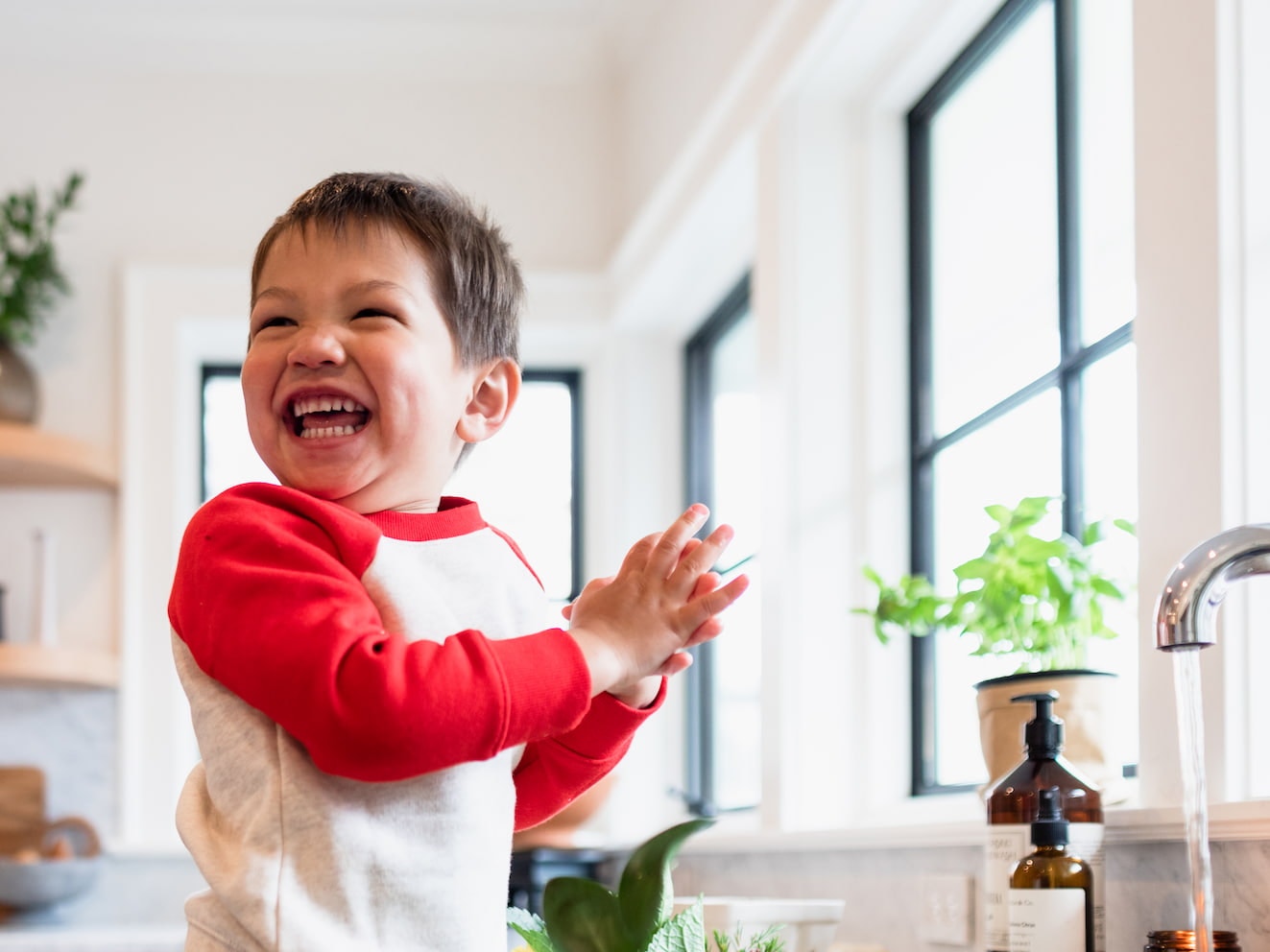 a smiling small boy in front of a kitchen sink with the light of a Pella casement window shining