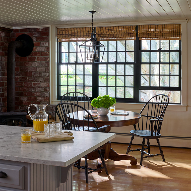 A cozy kitchen dining area featuring traditional wood windows, a round table, and black wooden chairs. 