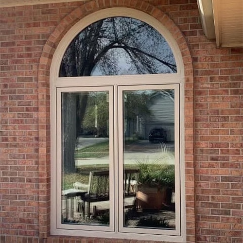 Two tan casement windows with an arched fixed window over the pair sits on a brick exterior wall.