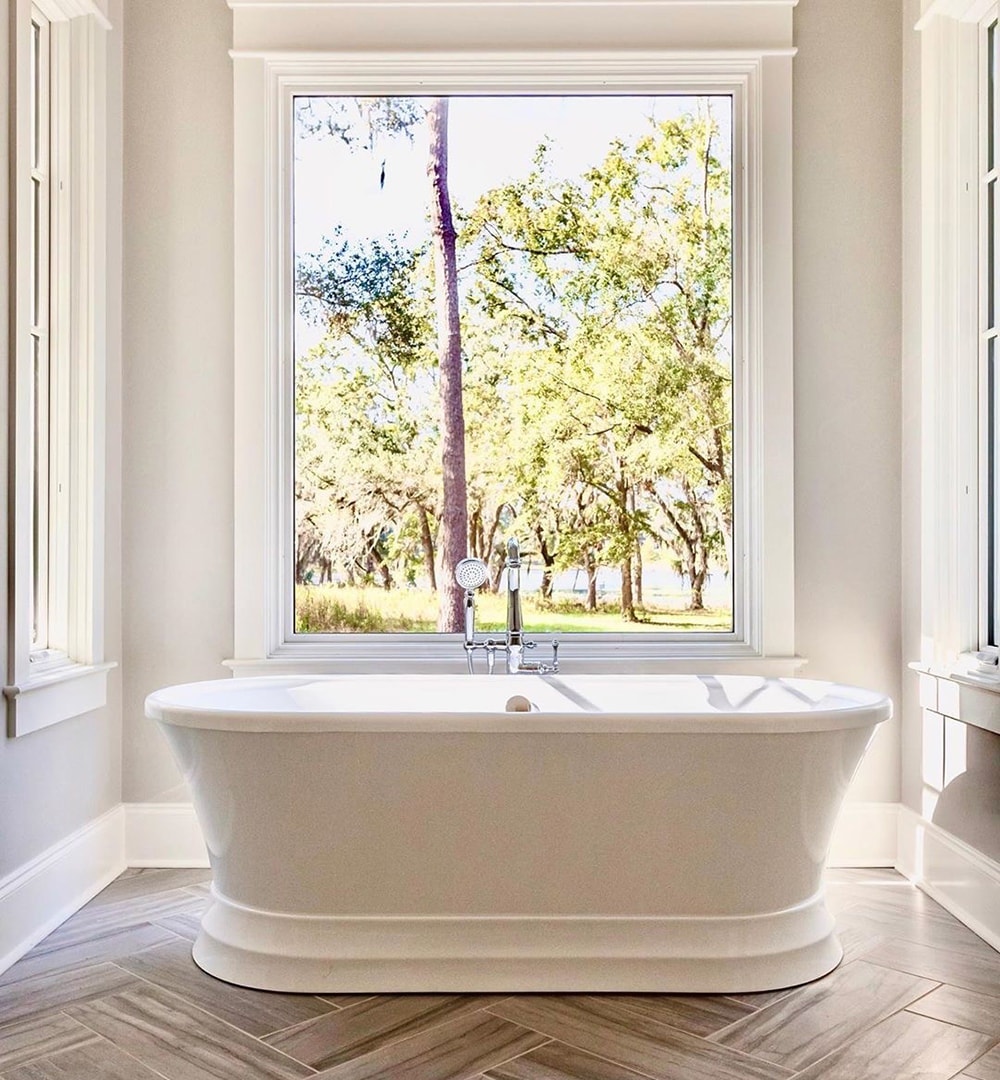 White bathroom window directly behind bathtub creates bright, picturesque space.