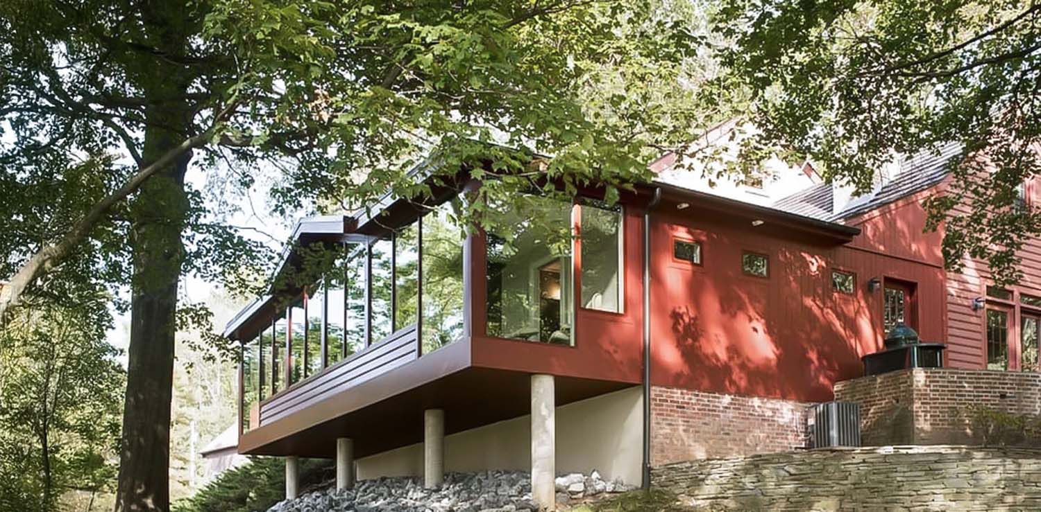 Red house with large windows and a brick foundation surrounded by trees in Harrisburg.