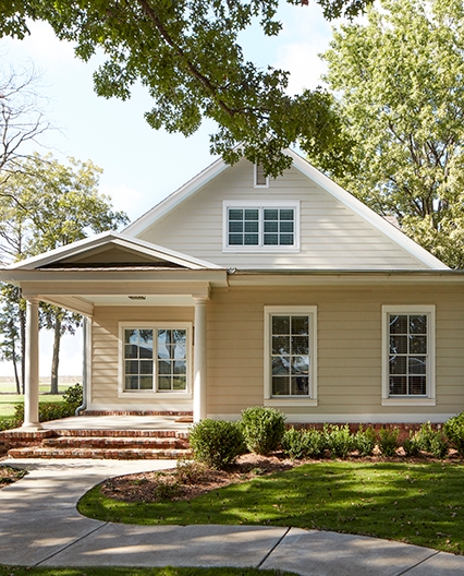 A yellow craftsman home with greenery around the home and white windows.
